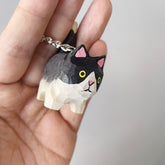 Hand-painted Holstein cat keychain with big yellow eyes, held in a hand to show scale and craftsmanship.